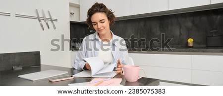 Portrait of young woman at home, working, writing in notebook, taking notes or doing homework.