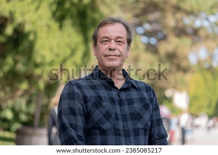 Portrait of a confident man of 45-50 years old on a neutral blurred background of a city park. Royalty-Free Stock Photo #2385085217