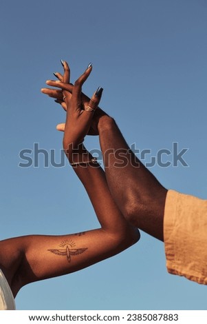 Anonymous ethnic couple while standing female with tattoo intertwining fingers of male and clasping hands together against cloudless blue sky in sunny daylight Royalty-Free Stock Photo #2385087883