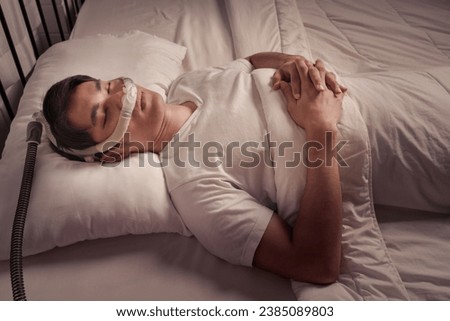 Peaceful Asian male asleep using CPAP mask and machine for obstructive sleep apnea and snoring remedy Royalty-Free Stock Photo #2385089803