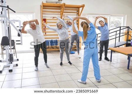 Group of senior people working out in fitness class of rehab center with female sports instructor Royalty-Free Stock Photo #2385091669