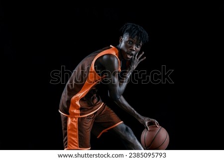 Portrait of young african man, basketball player training with ball isolated over black studio background. Concept of professional sport, healthy lifestyle, motion and action