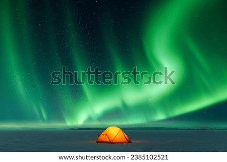 Orange tent lighted from the inside against the backdrop of incredible sky with Northern lights. Aurora borealis in winter field Royalty-Free Stock Photo #2385102521