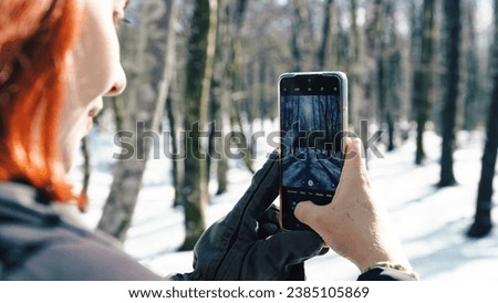 Young woman with gloves taking snow pictures with her phone 