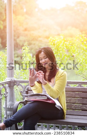 Beautiful young female university or college student smiling while holding a book, seated by a lake in a park.