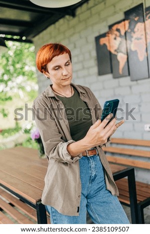 Redhead woman with short haircut holding mobile phone device in the yard house terrace