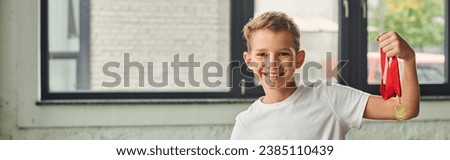cute preadolescent boy in sportswear holding golden medal smiling at camera, child sport, banner Royalty-Free Stock Photo #2385110439