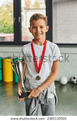 vertical shot of little cute boy with golden medal and trophy smiling at camera, child sport Royalty-Free Stock Photo #2385110503