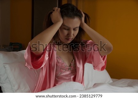 The Thai woman in a pink satin nightgown is experiencing insomnia on the bed during the night time. Royalty-Free Stock Photo #2385129779