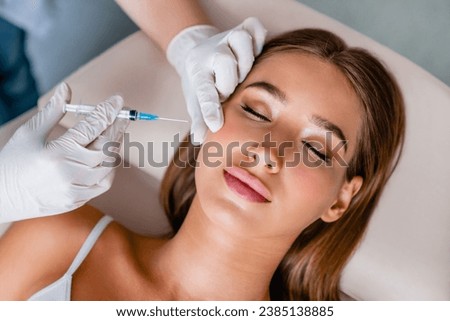 Young woman gets beauty facial injections in salon. Treatment, facial anti-age procedures. Cosmetologist hands in gloves doing shots with syringe Royalty-Free Stock Photo #2385138885