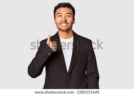 Young Chinese man in business suit in studio smiling and raising thumb up