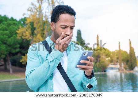 Student looking at the phone with a surprised expression outdoors in the campus park. High quality photo