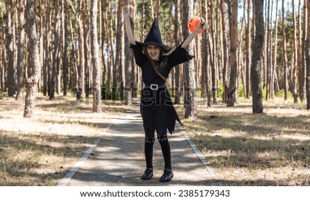 Kid going trick or treating. Low section shot of child in festive Halloween costume with cute jack-o-lantern. Child girl in witch costume holding orange pumpkin basket