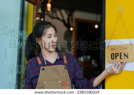business employee Barista staff Beautiful Asian girl The owner of a small coffee shop turned to look next to the welcome sign. to open the store in morning Change sign to tell customers that is open.