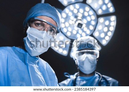 Surgeons in hospital operation theater. Serious confident doctors medical workers in protective blue gowns and face masks looking at the camera. Medical teamwork. Urgency Royalty-Free Stock Photo #2385184397