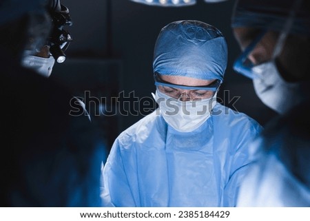 Concentrated surgeon team performing surgery, hospital operation looking at the patient. Plastic surgery, operation on heart, brain. Microsurgery concept Royalty-Free Stock Photo #2385184429