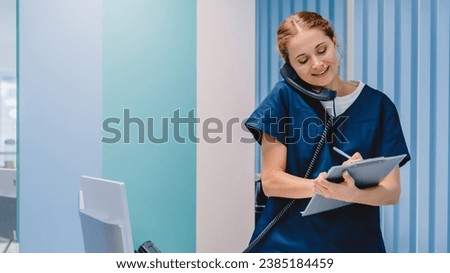 Caucasian female practitioner working at reception desk while answering phone calls and scheduling appointments in medical clinic. Hospital concept. Royalty-Free Stock Photo #2385184459