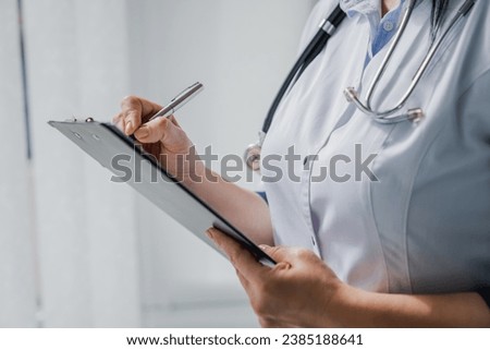 Female doctor with stethoscope writing prescription on clipboard. Cropped photo of nurse medical worker taking notes, noting diagnosis, test results, medical prescription, side effect of drugs history