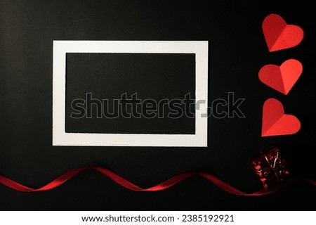 White photo frame and red heart paper pasted on a black background.