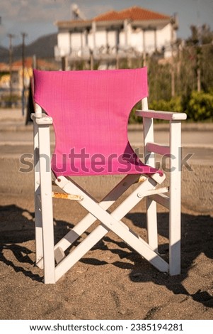 A solitary pink canvas chair sits abandoned on a serene Greek beach, bathed in the golden light of the setting sun, offering a peaceful spot for contemplation.