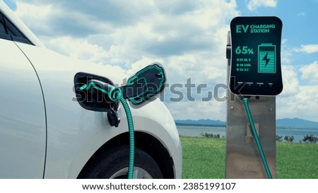 Electric car plugged in with charging station to recharge battery by EV charger cable with nature and lake background. Future innovative ev car and energy sustainability. Peruse