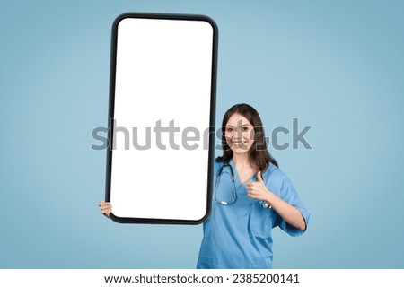 Cheerful female nurse in blue scrubs holding large mock-up smartphone screen for advertising medical content or offer, blue background