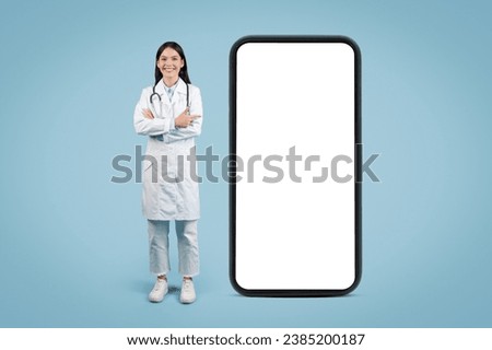 Female doctor in uniform standing near big blank cellphone for medical custom graphics and text, banner, place for design