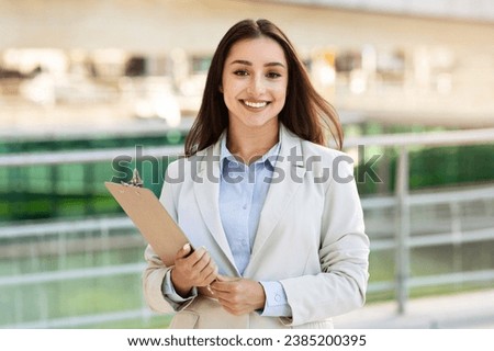 Smiling pretty confident young woman secretary manager in suit with clipboard enjoy work, in city outdoors, close up. Business, startup, study and lifestyle planning, ad and offer