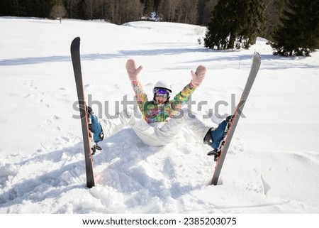 young woman or teenage girl in good mood while skiing fell and lies cheerfully in the snow. enjoying the moment, digital detox, positive thinking. Interesting active winter holiday, healthy lifestyle Royalty-Free Stock Photo #2385203075