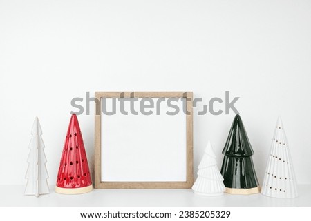 Christmas mock up with wooden frame and tree decor. Square frame on a white shelf against a white wall. Copy space.