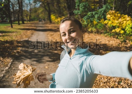 Beautiful girl taking picture of herself while walking in a sunny autumn forest. Adventure, travel, holiday concept.