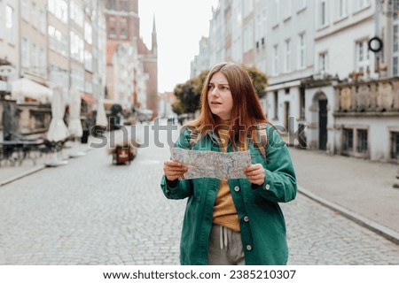 Portrait beautiful woman with paper map on urban street. Young worried female traveler lost in the city using map. Vacation concept by exploring interesting places to travel. Royalty-Free Stock Photo #2385210307
