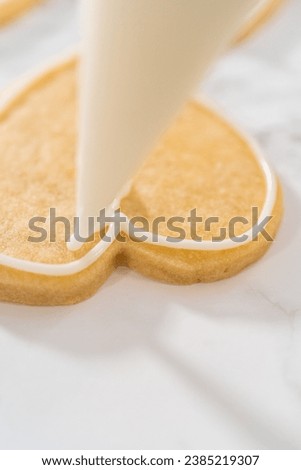 Decorating heart-shaped sugar cookies with pink and white royal icing for Valentine's Day. Royalty-Free Stock Photo #2385219307