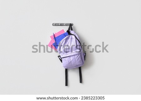 School backpack with stationery hanging on light wall