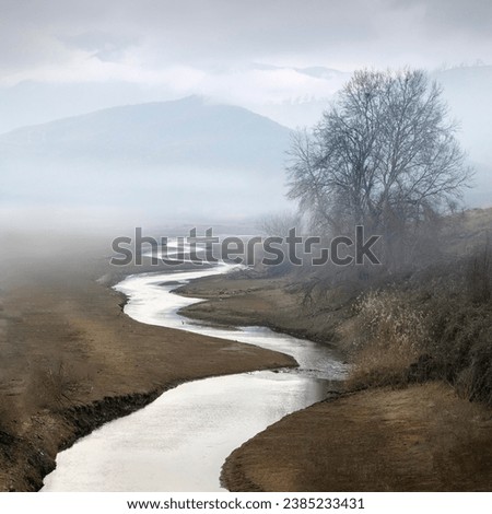 A photograph of a small river meandering through the fields toward the misty background Royalty-Free Stock Photo #2385233431