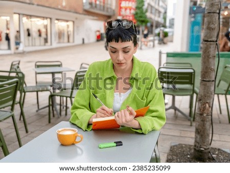 woman  student writing in a notebook, making a plan at the street cafe in city. Concept of study hard  Lifestyle photo Royalty-Free Stock Photo #2385235099