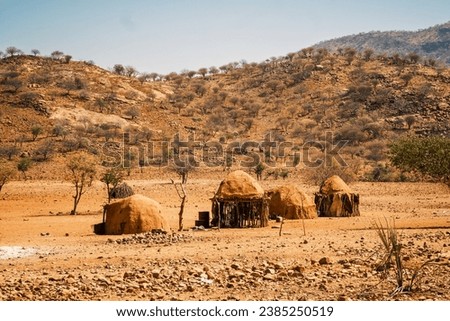 Traditional Himba village with mud and wood huts, north of Opuwo, Kunene Region, Namibia. The Himba are a semi-nomadic remote African tribe and their lives are centered around cattle. Royalty-Free Stock Photo #2385250519