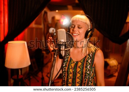 A young, talented musician singing into a condenser microphone in a music studio. She is singing from heart, enjoying the process, letting go of emotions. Alternative, fashionable, focused.