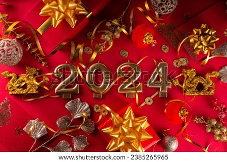 Chinese New Year 2024 greeting card. Bright red asian year of the dragon background with golden dragon figurine, Chinese lanterns, traditional jewelry, gifts, coins, cookies with wishes, copy space Royalty-Free Stock Photo #2385265965