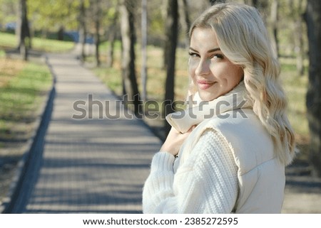 Portrait of a young beautiful blonde with long hair in a white sweater and jacket on a sunny autumn walk in the city