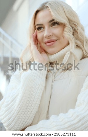 Portrait of a young beautiful blonde with long hair in a white sweater and jacket on a sunny autumn walk in the city