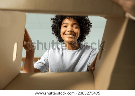 Inside of cardbox bottom view. African girl unpacking delivery looking in box. Woman opening carton box. Female getting parcel looking at delivered goods items. Satisfied client positive feedback Royalty-Free Stock Photo #2385273495