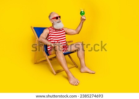 Full length portrait of positive grandfather sit lounger hand hold raise alcohol drink glass isolated on yellow color background