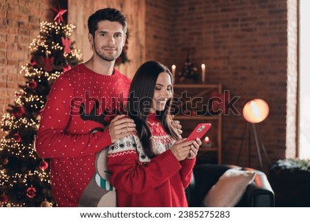 Photo of young two lovers using smartphone to order christmas presents online website stay home warm clothes on garland background indoors