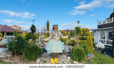 A cheerful girl is jumping in nature in her garden in the fall, dressed in a jacket, with a coastal garden around.