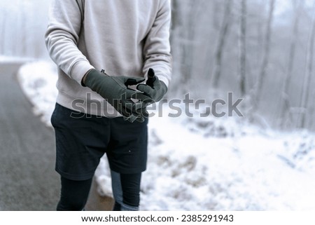 Picture of a man's hands, wearing gloves and sports clothes.Warm up before going on a run in the foods on a snowy winter day, trees and ground are cover in snow
