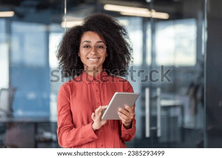 Portrait young successful businesswoman with tablet computer in hands inside office at workplace, female programmer testing new software smiling looking at camera satisfied with achievement results.