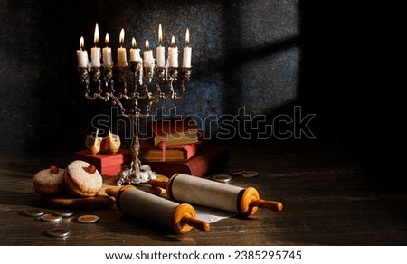 Hanukkah (traditional candelabra), doughnut, dreidel with Hebrew letters (N, H, F), Religious books (Tanakh) and scroll Tanakh on a dark background Royalty-Free Stock Photo #2385295745