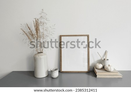 Elegaant interior, home office. Blank wood picture frame mockup. Cup of coffee, pencils and little pumpkins. Vase with dry grass. Autumn boho home decor. White wall background. Grey table, desk.