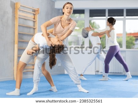 Concentrated young woman applying inverted headlock, painful control grip to hold female opponent during mock bout in self-defense training..